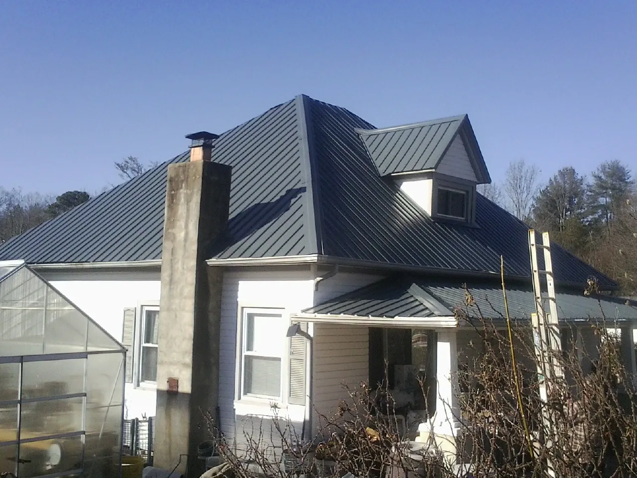 Dark blue standing seam metal roof on a white farmhouse with dormer — Slate & Tile Roof Repair by Roofing Brothers in Minneota