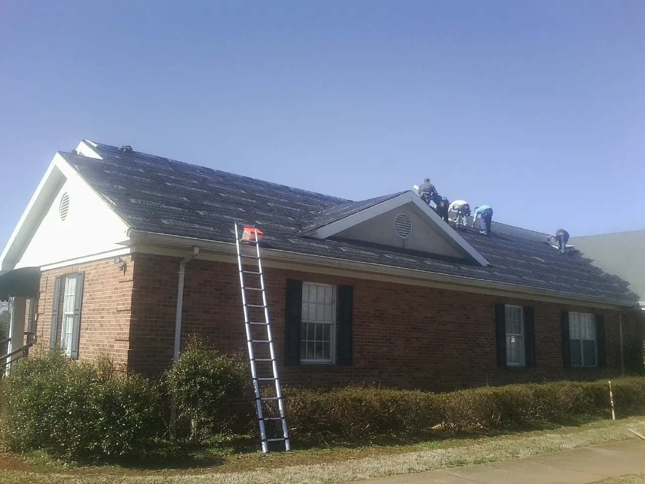Crew tearing shingles off a brick ranch roof with a ladder set — Metal Roof Repair work by our crew in Minneota