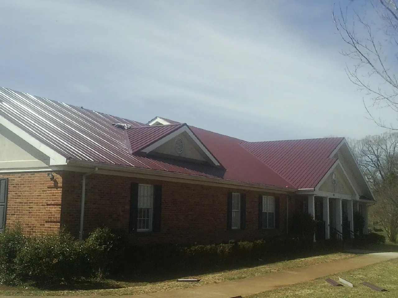 Red metal roof with gabled entries on a long brick building, from a Hail Damage Roof Repair job in Minneota