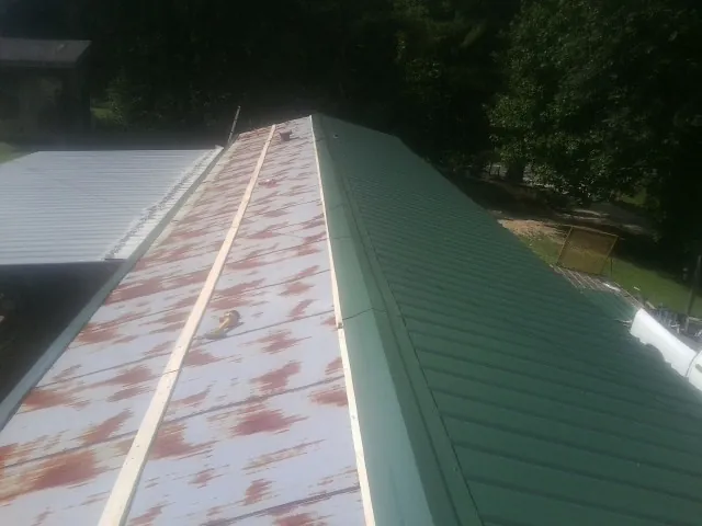 Old rusted panels beside newly installed green metal roofing — Wind Damage Roof Repair by Roofing Brothers in Minneota