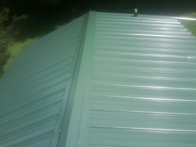 New green metal panels meeting at the ridge of a roof — Flat Roof Repair work by our crew in Minneota