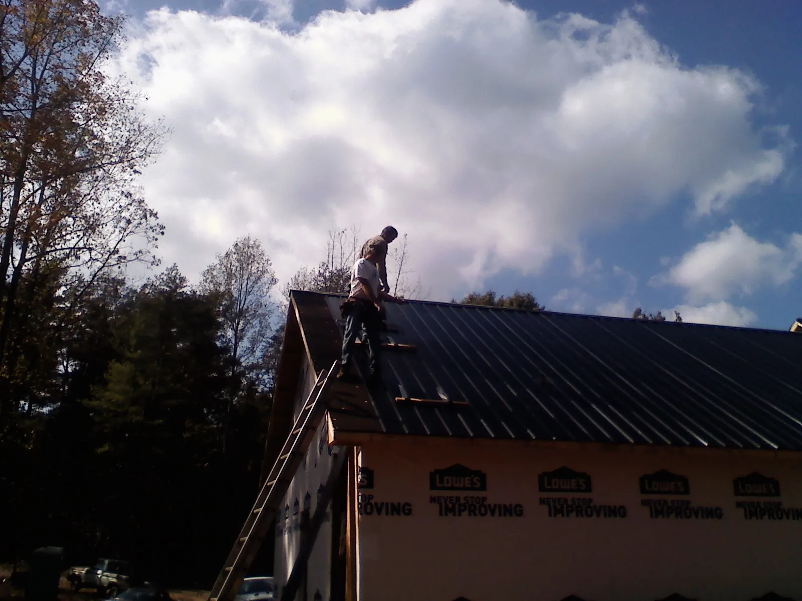 Roofer fastening dark metal panels high against a cloudy sky, from a Roof Inspection job in Minneota