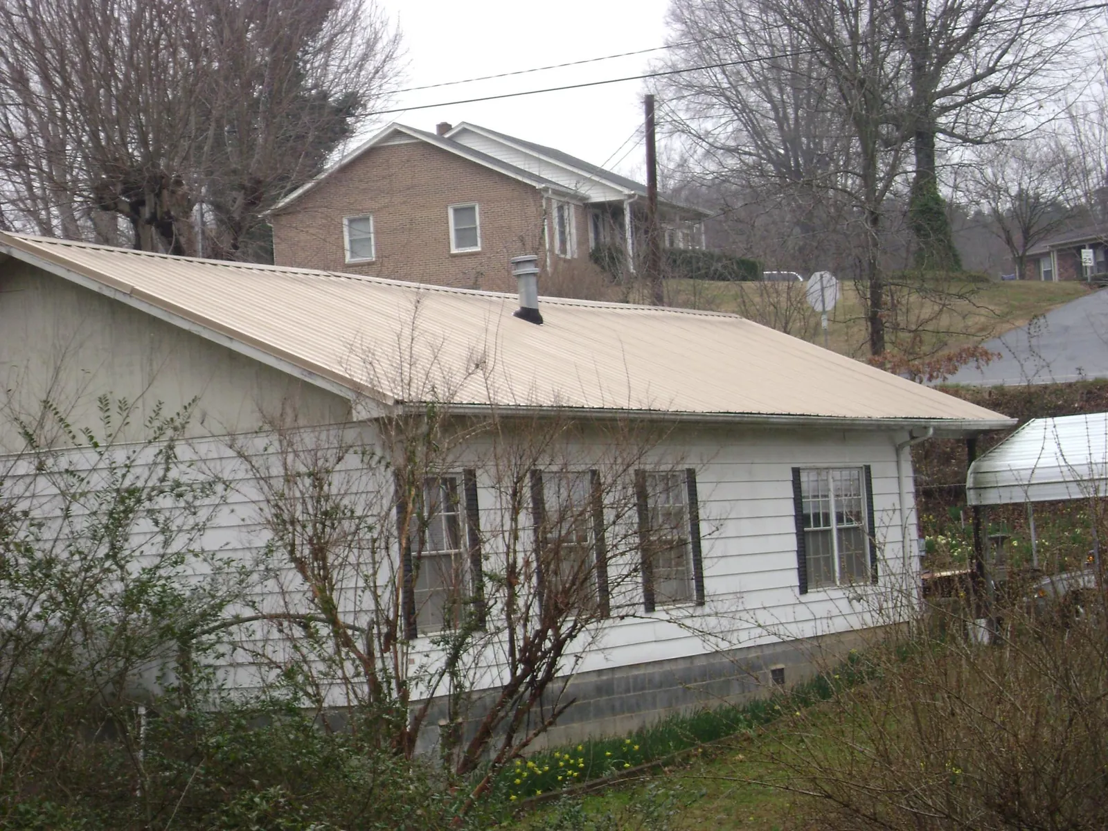 Tan metal roof on a white sided house set into a hillside — Commercial Roofing by Roofing Brothers in Minneota
